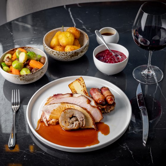 Meat with assortment of side dishes served on a black table with a glass of red wine
