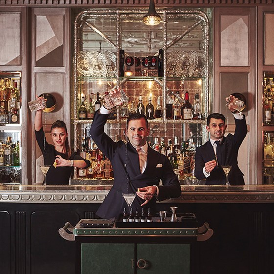 The Connaught Bar. Three bar tenders pour cocktails behind a bar.