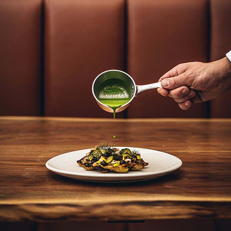 A colourful dish in a white plate with sauce being poured on it.