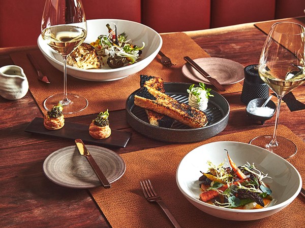 Carrot and vegetable dish, glasses of wine, and fish dish laid out on table